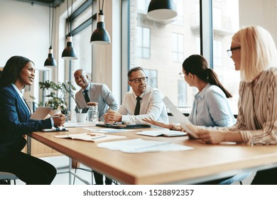 Group of diverse businesspeople smiling while discussing paperwork together during a meeting around a table in a modern office - Shutterstock ID 1528892357