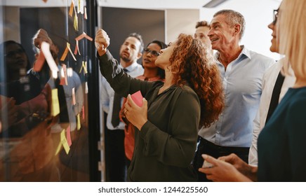 Group of diverse businesspeople strategizing with sticky notes on a glass wall while working together in a modern office - Powered by Shutterstock