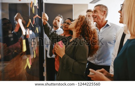 Group of diverse businesspeople strategizing with sticky notes on a glass wall while working together in a modern office