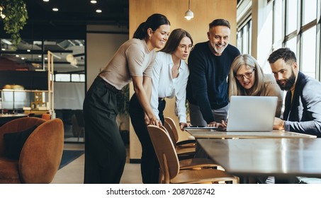 Group of diverse businesspeople using a laptop while collaborating on a new project. Team of happy businesspeople looking at the laptop screen while working together in a modern workspace.