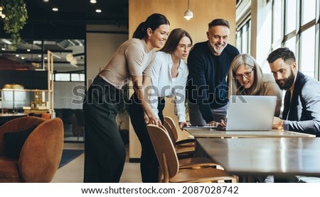 Group of diverse businesspeople using a laptop while collaborating on a new project. Team of happy businesspeople looking at the laptop screen while working together in a modern workspace.