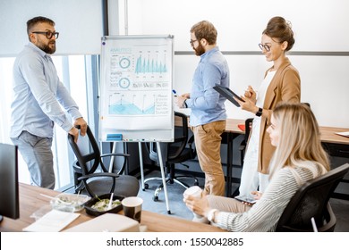 Group Of Diverse Colleagues Discussing Some Working Momets With Presentation On Flipchart During A Small Conference In The Office