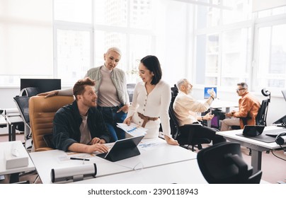 Group of diverse colleagues discussing work at table with laptop and papers in office - Powered by Shutterstock