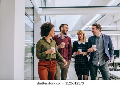 Group of diverse coworkers walking through a corridor in an office, holding paper cups - Shutterstock ID 1126812173