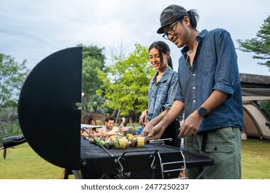 Group of diverse friend having outdoors camping party together in tent. Attractive young man and woman traveler cooking foods barbecue, enjoy hanging out during holiday vacation trip in wood forest. - Powered by Shutterstock