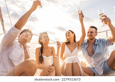 Group of diverse friends drink champagne while having a party in yacht. Attractive young men and women hanging out, celebrating holiday vacation trip while catamaran boat sailing during summer sunset.