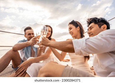 Group of diverse friends drink champagne while having a party in yacht. Attractive young men and women hanging out, celebrating holiday vacation trip while catamaran boat sailing during summer sunset. - Shutterstock ID 2300284371