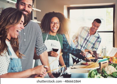 Group of diverse friends drinking and cooking in front of long food preparation table indoors - Powered by Shutterstock