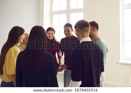 Group of diverse friends gather together in club meeting. Smiling convincing friendly coach talking to team of multiethnic people, suggesting interesting idea, teaching to play funny ice breaker game