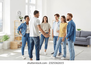 Group of diverse friends having a discussion. Several young multiracial people standing in the living room at home and listening to a young man talking about something - Powered by Shutterstock