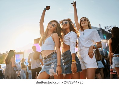 Group of diverse girls having fun at coastal music festival. Women dance, smile in sunlight by sea. Friends enjoy live band, sunset party vibes on sandy beach. Youth culture, summer event gathering. - Powered by Shutterstock