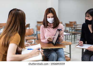 Group of diverse international students wearing protective  masks and talking, discussing the project, sitting at the desk in the classroom at the university
