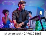 Group of diverse man and woman dancing with DJ mixing music on console. Attractive young teenager friends having fun with DJ mixing and scratching music mixer controller at house party with neon light