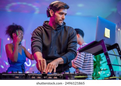 Group of diverse man and woman dancing with DJ mixing music on console. Attractive young teenager friends having fun with DJ mixing and scratching music mixer controller at house party with neon light