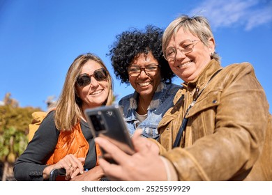 Group of diverse mature women smiling looking and using smartphone on a street. Middle-aged female friends searching a places on mobile and enjoying vacations on a autumn sunny day - Powered by Shutterstock