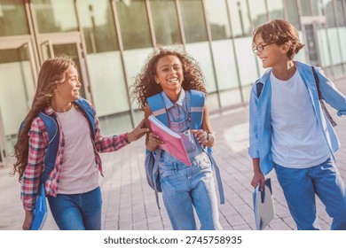 Group of diverse multiethnic elementary middle school kids friends boys and girls happy kids classmates walking and laughing having fun together with backpacks near school building after lessons