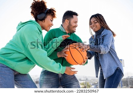 A group of diverse and multi-ethnic friends gather on a basketball court. The two black girls try to take the ball away from the black boy in the middle. Concept of multi-ethnic social activities.