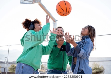 A group of diverse and multi-ethnic friends gather on a basketball court. The 3 young men try to catch the ball that is in the air. Concept of multi-ethnic sports activities.