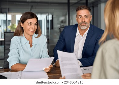 Group of diverse partners mature Latin business man and European business women discussing project with documents at table in office. Team of colleagues professionals business people working together. - Powered by Shutterstock