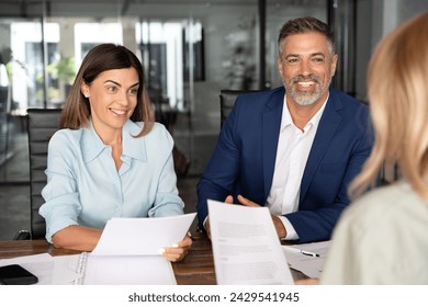 Group of diverse partners mature Latin business man and European business woman have meeting, discussing documents at table in office. Team of colleagues professionals businesspeople working together. - Powered by Shutterstock