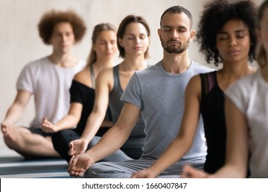 Group of diverse people meditating together visualizing during yoga morning session, focus on Caucasian man seated cross-legged in row with associates, no stress, spiritual practise, lifestyle concept - Powered by Shutterstock