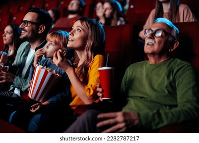 A group of diverse people are in a movie theater enjoying a movie, having popcorn and drinks. - Powered by Shutterstock