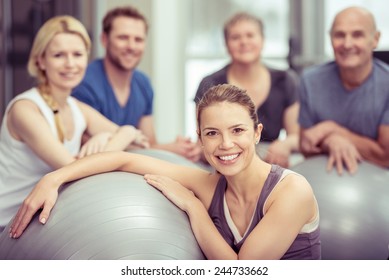 Group of diverse people in a pilates class at a gym posing with their gym balls looking at the camera with focus to an attractive young woman in the foreground - Powered by Shutterstock