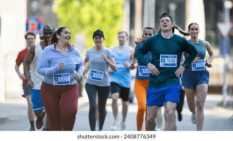 Group of Diverse People Running in a Marathon with the Cheers of their Loved Ones and Supporters in the Audience. Runners Participating in a Charity Run to Raise Money a Cause - Powered by Shutterstock