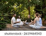 Group of diverse people sitting in a circle and meditating outside in a peaceful green forest. Men and women practicing mindfulness and deep breathing together on a wooden platform in nature.