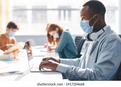 Group Of Diverse People Sitting At The Table, Working, Studying For Test, Making Project Or Homework Together, Wearing Surgical Masks. African American Man With Headphones Using Laptop At Workplace