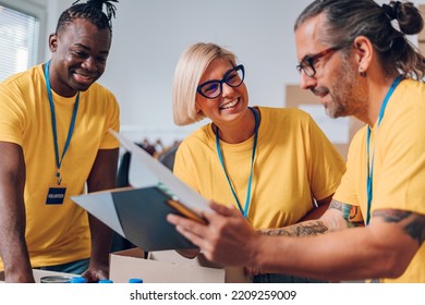 Group Of Diverse People Working In Charitable Foundation. Happy Volunteer Separating Donation Stuff. Social Workers Making Check List Of The Thins That Are Done. Copy Space. Working As A Team.