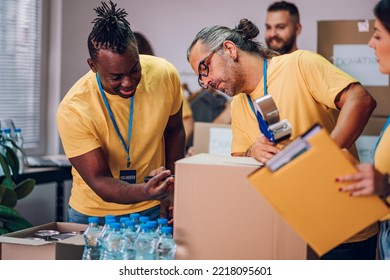 Group Of Diverse People Working In Charitable Foundation. Happy Volunteer Separating Donation Stuff. Focus On An African American And Caucasian Middle Aged Man Sorting Donations During Food Drive.