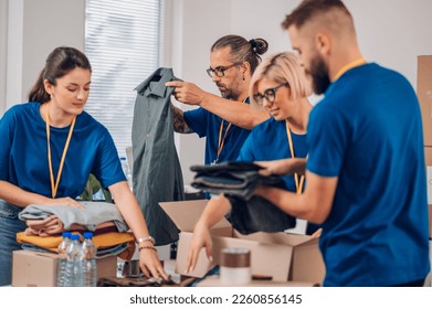 Group of diverse people working in charitable foundation. Volunteer separating donation stuff. Volunteers sort donations during food drive. Focus on a middle aged man preparing clothes. Copy space. - Powered by Shutterstock