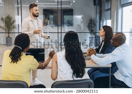 Group of diverse professionals collaborating on sustainable energy solutions, presenting a wind turbine prototype in a modern office meeting