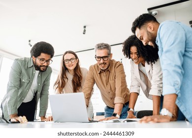 A group of diverse professionals is standing around a laptop, highlighting a moment of team collaboration and digital strategy planning, solving project tasks, or analyzing the result - Powered by Shutterstock