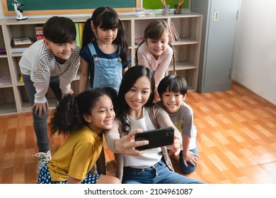 Group Of Diverse School Kids And Asian Young Woman Teacher Taking Selfie With Mobile Phone Or Smartphone.