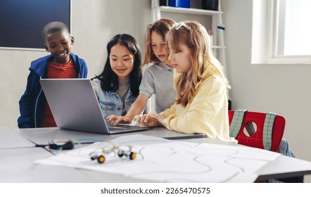 Group of diverse school kids learning how to program robots using a laptop. Elementary school students developing coding skills to control robot cars in a hands-on computer science lesson. - Powered by Shutterstock