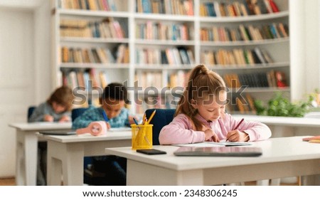 Group of diverse schoolboys and schoolgirl sitting at desks in classroom at primary school, writing or drawing in notebook. Reopening and return back to school