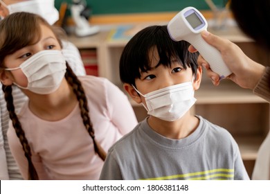 Group Diverse Students In School Building Checked And Scanned For Temperature Check. Elementary Pupils Are Wearing A Face Mask And Line Up Before Entering Into Classroom. Covid19 School Reopen Concept