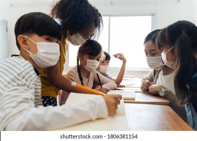 Group Of Diverse Students In School Building Discussing In Group Study Class. Elementary Pupils Are Wearing A Face Mask While Brainstorming. Covid-19 School Reopen Concept