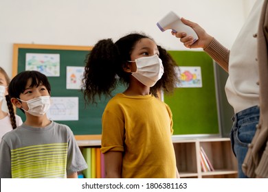 Group Diverse Students In School Building Checked And Scanned For Temperature Check. Elementary Pupils Are Wearing A Face Mask And Line Up Before Entering Into Classroom. Covid19 School Reopen Concept