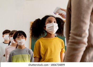 Group diverse students in school building checked and scanned for temperature check. Elementary pupils are wearing a face mask and line up before entering into classroom. Covid19 school reopen concept - Powered by Shutterstock