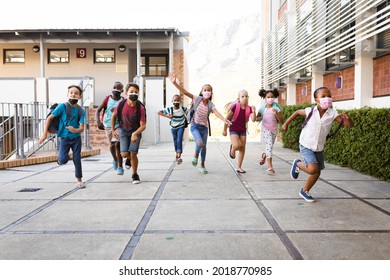 Group Of Diverse Students Wearing Face Masks Running At Elementary School. Education Back To School Health Safety During Covid19 Coronavirus Pandemic.