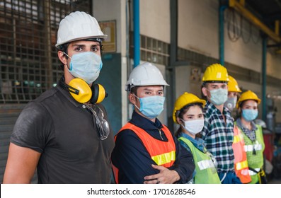 Group of diverse team of workers wearing face mask and protective helmets standing in front of the factory