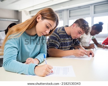 Group of diverse teenage students writing in class or during an exam. Back to school, exam, classes, high school
