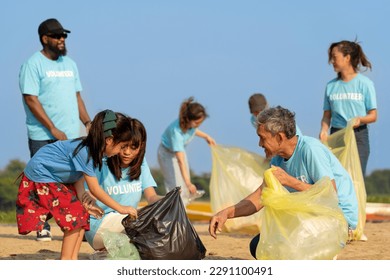 group of diverse volunteers charitable working together to clean up river beach, senior adult and girls picking trash into garbage bags separating reused plastic for recycling waste management - Powered by Shutterstock