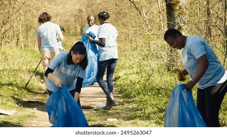 Group of diverse volunteers collecting rubbish from the woods and recycling in a garbage disposal bag, litter cleanup responsibility. Ecology activists picking up trash and plastic waste. Camera A. - Powered by Shutterstock