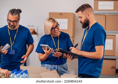 Group of diverse volunteers wearing blue volunteer t shirt at donations stand separating donation stuff and putting them in a cardboard boxes and using a tablet. Concept of a charitable foundation. - Powered by Shutterstock