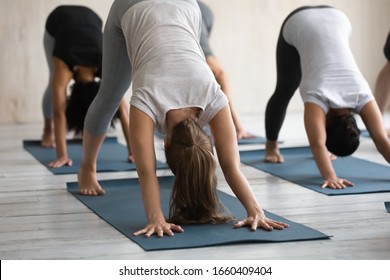 Group of diverse women in comfy sportswear do Downward Facing Dog or Adho Mukha Shvanasana work out together during yoga class session at sport club, asana energizes strengthens body, wellness concept
