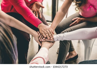 Group of diverse women put their hands together in stack empowering each other in breast cancer awareness campaign meeting